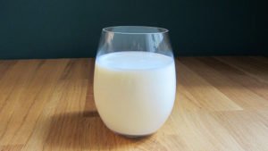 Vaso de cristal lleno de leche sobre encimera de madera