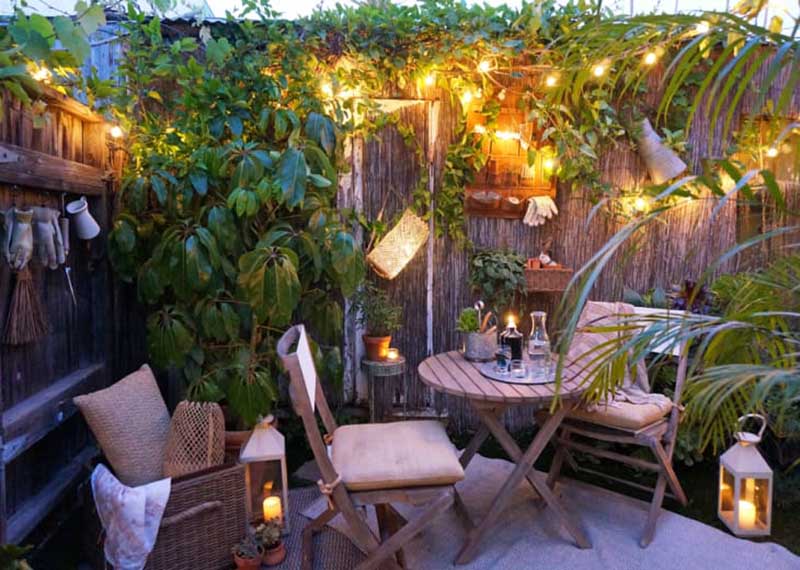 Un rincón de un jardín pequeño con muebles de madera iluminado con guirnaldas de luces